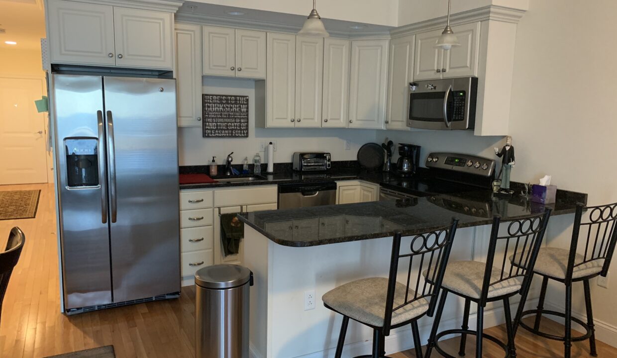 a kitchen with a stainless steel refrigerator and a black counter top.
