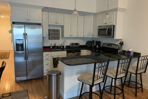 a kitchen with a stainless steel refrigerator and a black counter top.