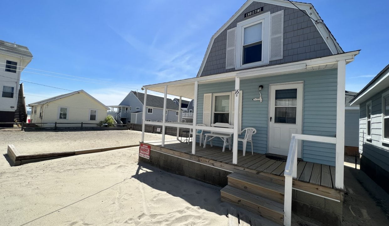 a small blue house with a porch on the beach.