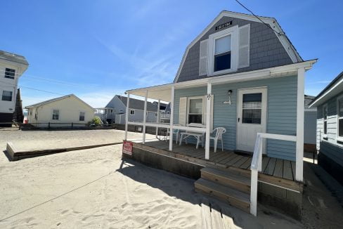 a small blue house with a porch on the beach.