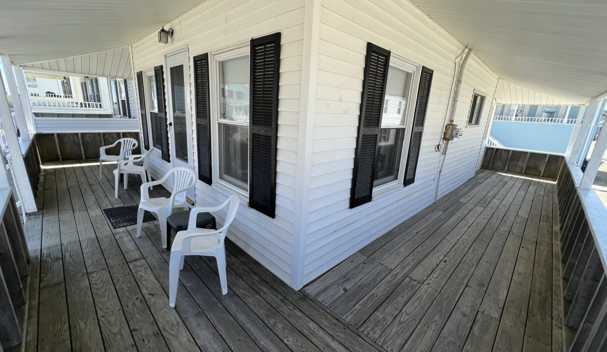 a porch with white chairs and black shutters.