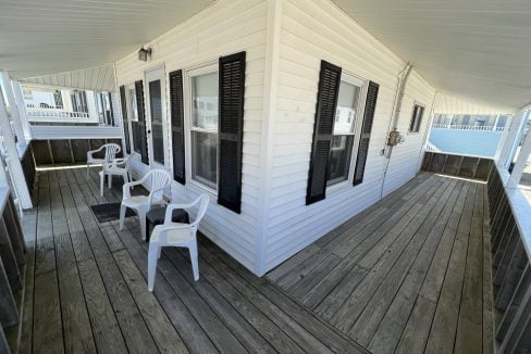 a porch with white chairs and black shutters.