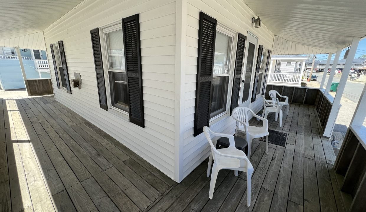 a porch with white chairs and black shutters.