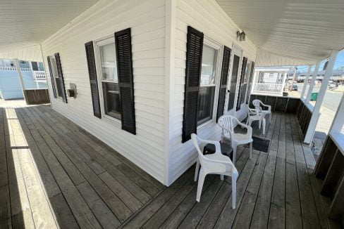 a porch with white chairs and black shutters.