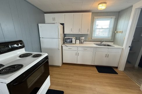 Small kitchen with white cabinets, a refrigerator, electric stove, microwave, coffee maker, sink, and a window letting in natural light.