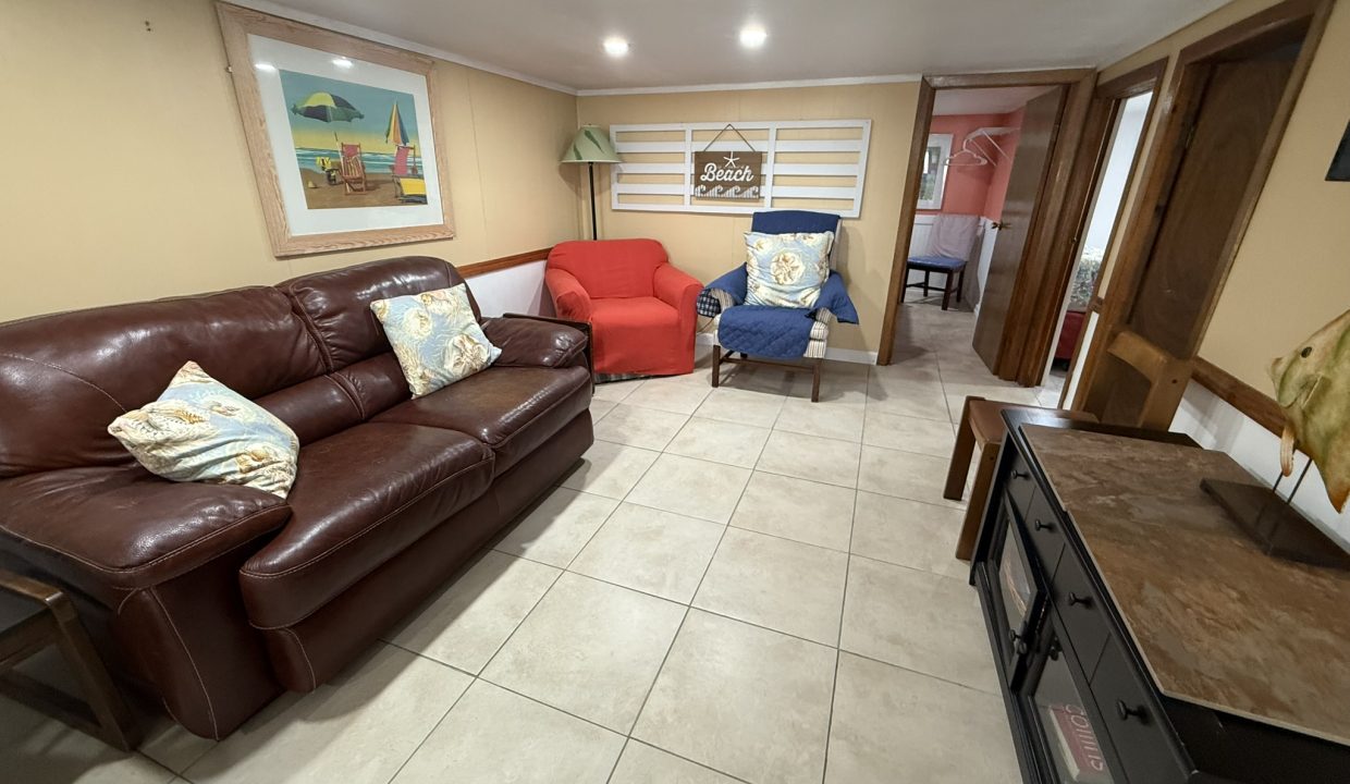 A living room with a brown leather sofa, red and blue armchairs, tiled floor, wall art, and a TV stand with a fish decoration.