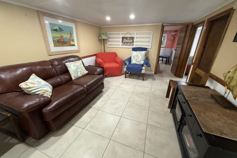 A living room with a brown leather sofa, red and blue armchairs, tiled floor, wall art, and a TV stand with a fish decoration.