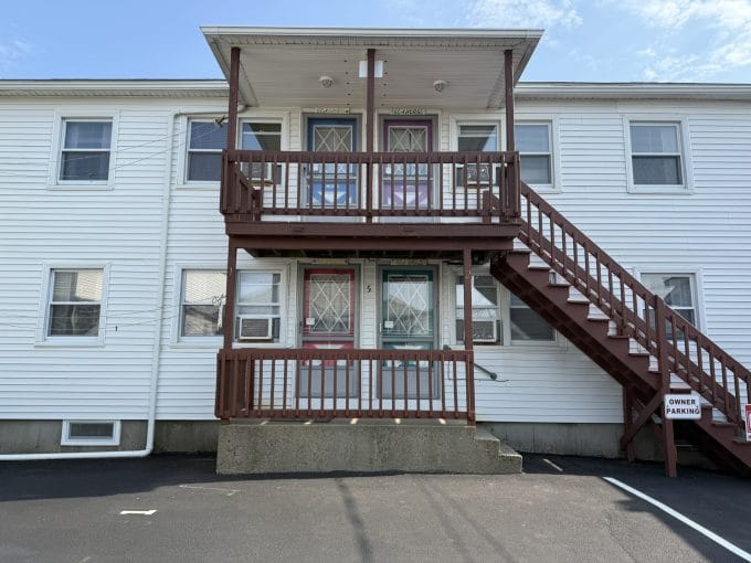 Two-story white apartment building with a central staircase, two doors on each level, and a sign marking "Owner Parking" on the right.