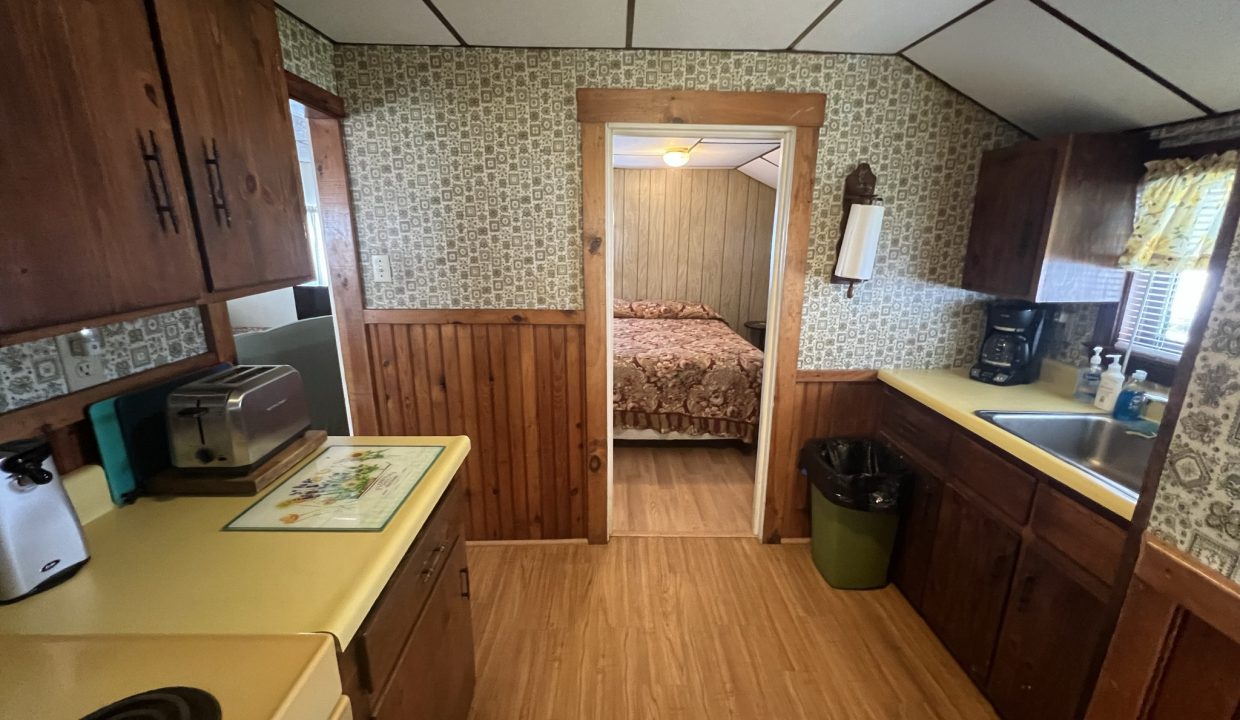 a kitchen with a sink, stove, microwave and a bed.