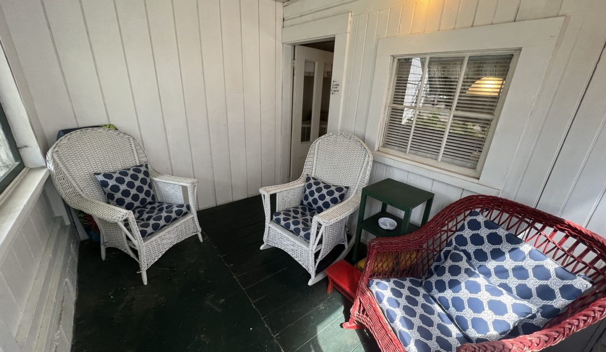 two wicker chairs sitting on a porch next to a window.