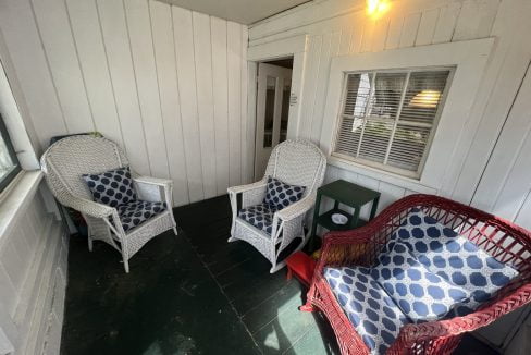 two wicker chairs sitting on a porch next to a window.