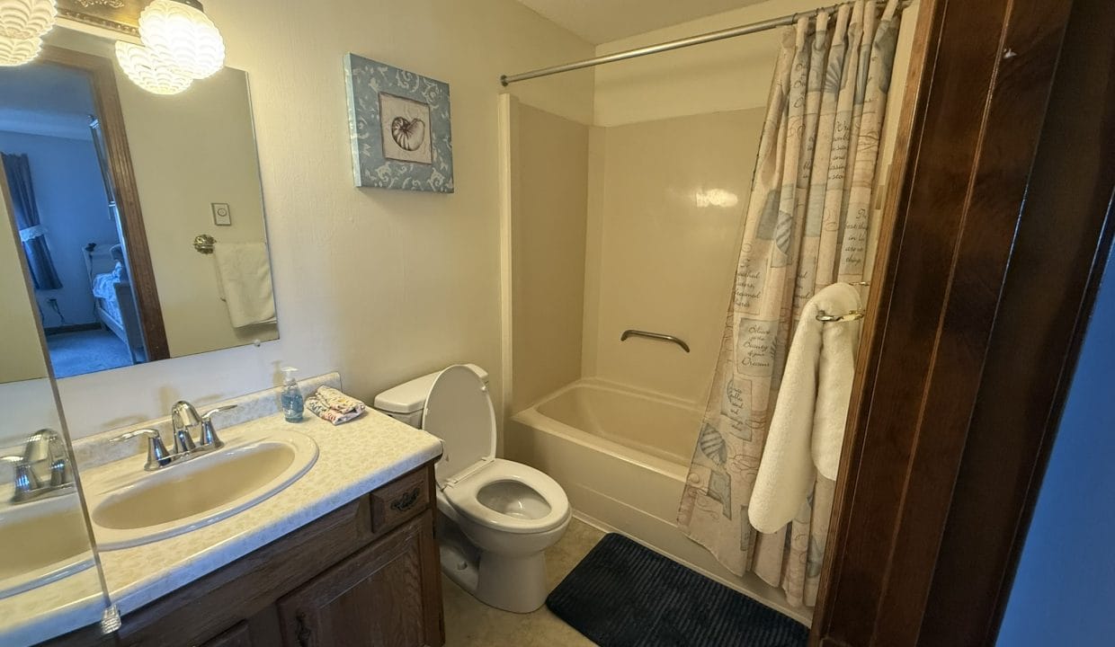 A small bathroom with a sink, mirror, toilet, bathtub with shower curtain, towel, and blue floor mat.