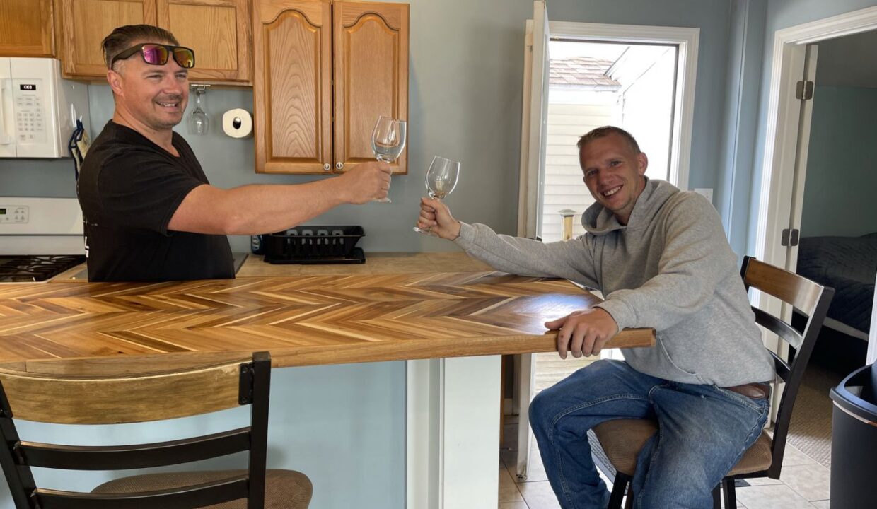 a couple of men sitting at a bar with wine glasses.