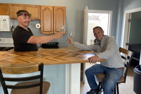 a couple of men sitting at a bar with wine glasses.