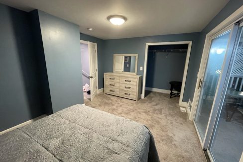 a bedroom with a bed, dresser, and sliding glass doors.