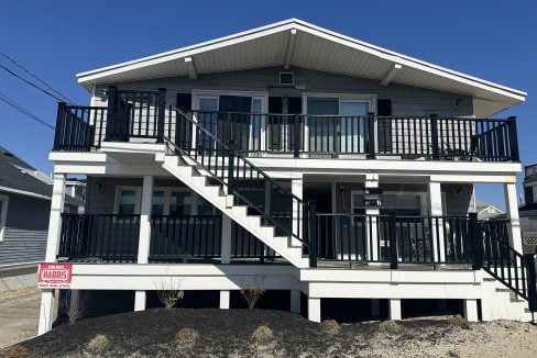 Two-story house with a black balcony railing and an external staircase leading to the upper floor.