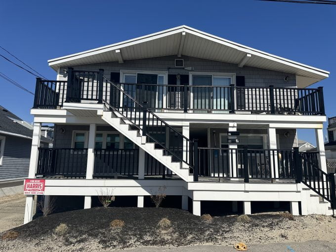 Two-story house with a black balcony railing and an external staircase leading to the upper floor.