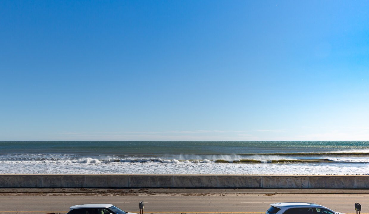 two cars parked in a parking lot next to the ocean.