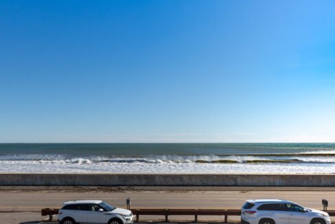 two cars parked in a parking lot next to the ocean.