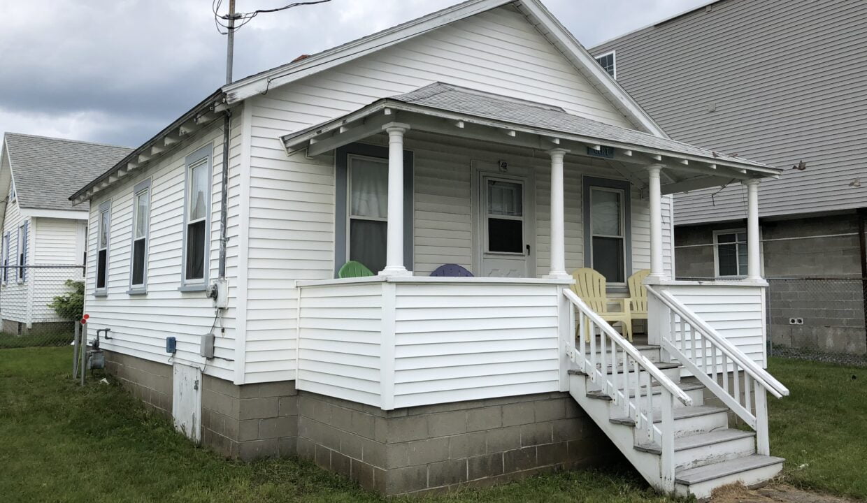 a small white house with a porch and stairs.