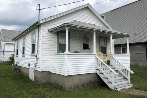 a small white house with a porch and stairs.