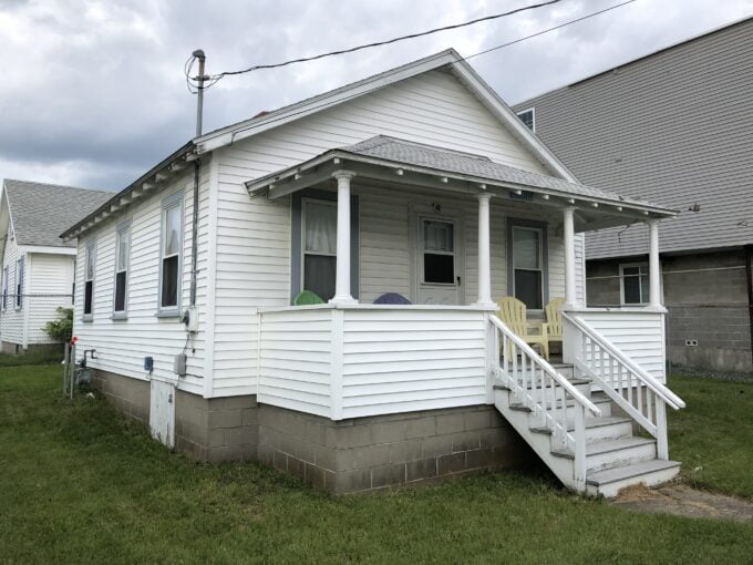 a small white house with a porch and stairs.