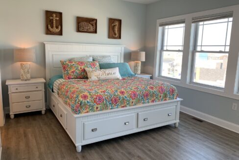 a bedroom with a bed, dressers, and two windows.