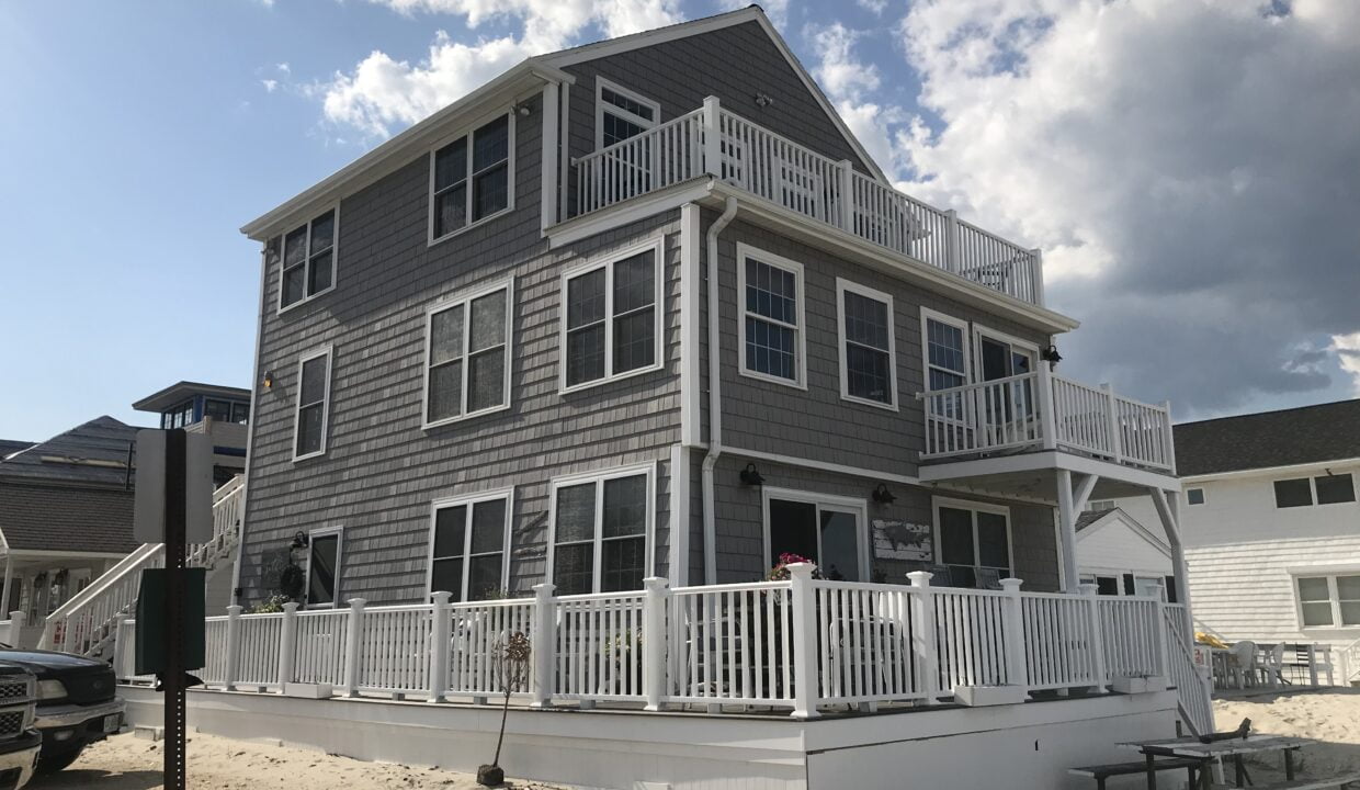 a beach house with a deck and a car parked in front of it.