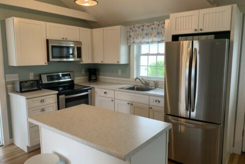 a kitchen with a refrigerator, stove, sink, and stools.