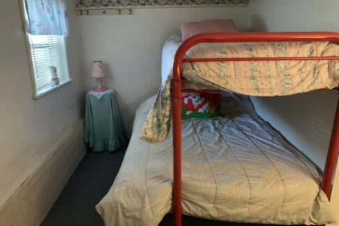a red metal bunk bed sitting in a bedroom next to a window.