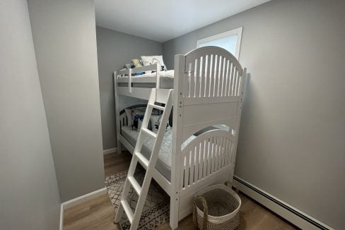 a white bunk bed sitting in a bedroom next to a window.