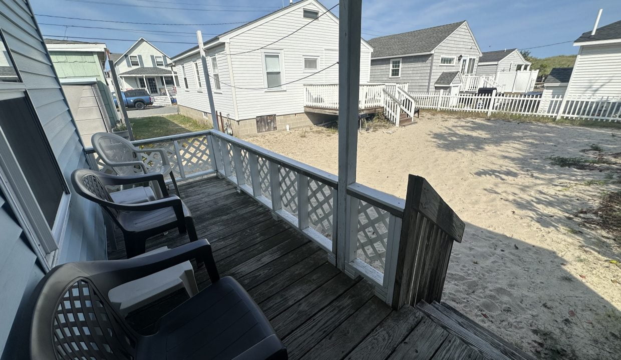 A porch with two chairs and a sand beach.