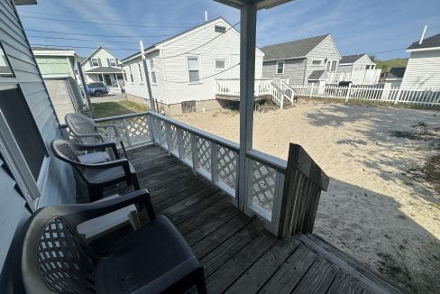 A porch with two chairs and a sand beach.