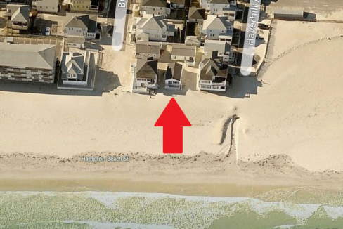 an aerial view of a beach with houses and a red arrow.