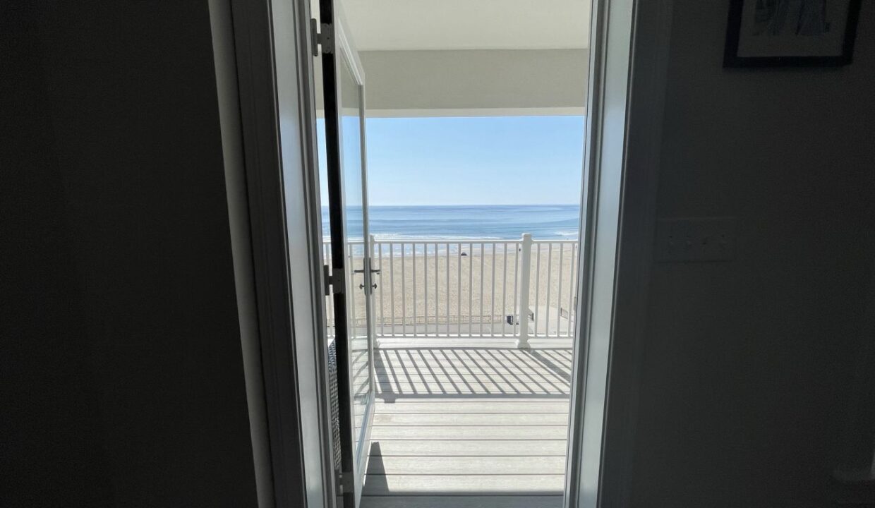 an open door leading to a balcony with a view of the ocean.