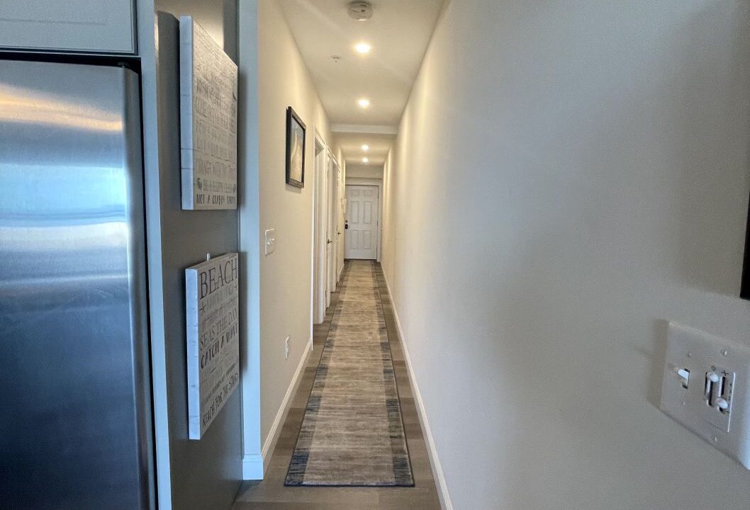 a long hallway leading to a kitchen with a refrigerator.
