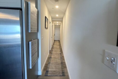 a long hallway leading to a kitchen with a refrigerator.