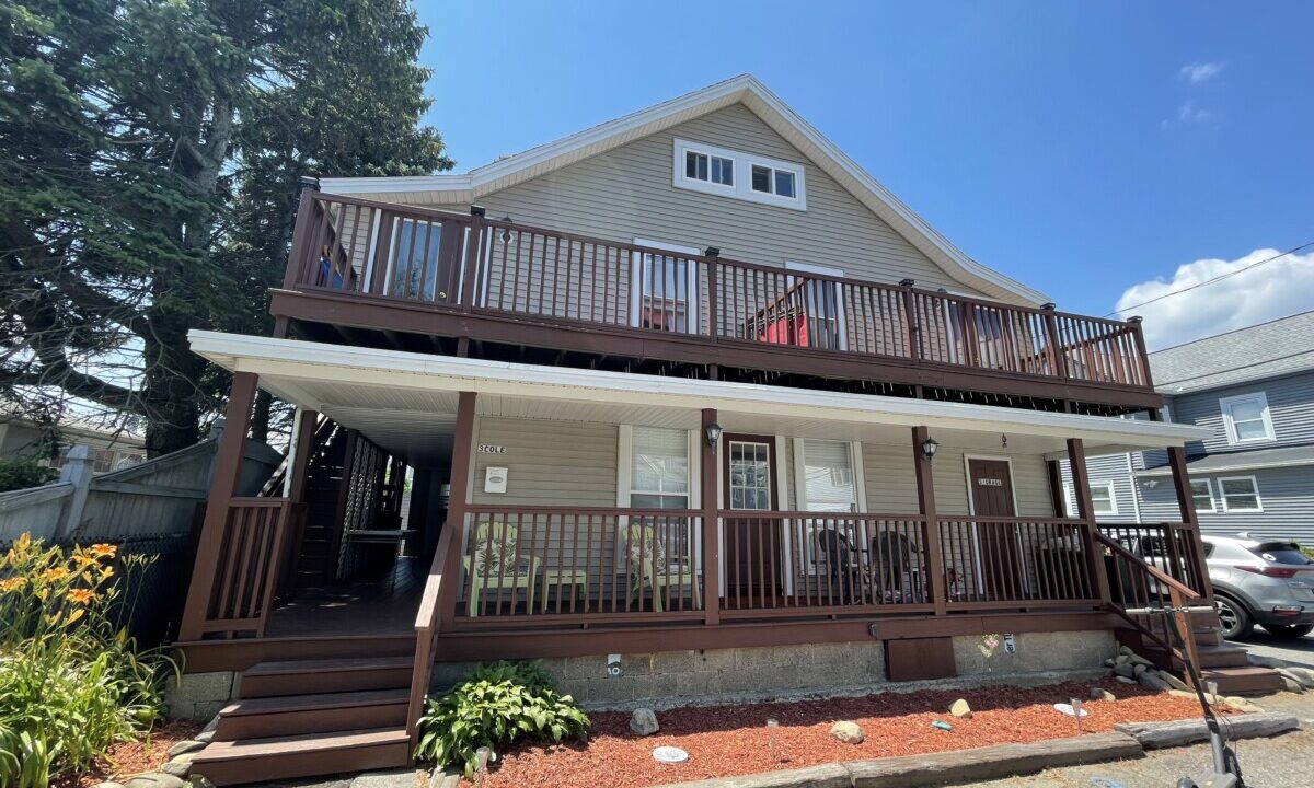 a two story house with a deck and a car parked in front of it.
