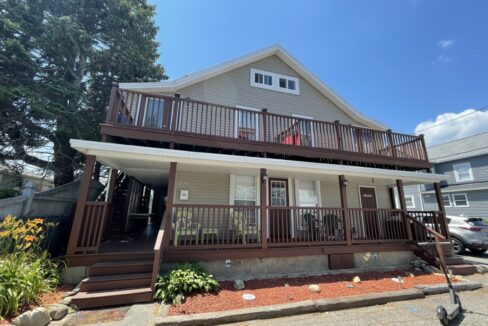 a two story house with a deck and a car parked in front of it.