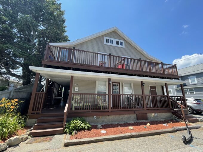 a two story house with a deck and a car parked in front of it.