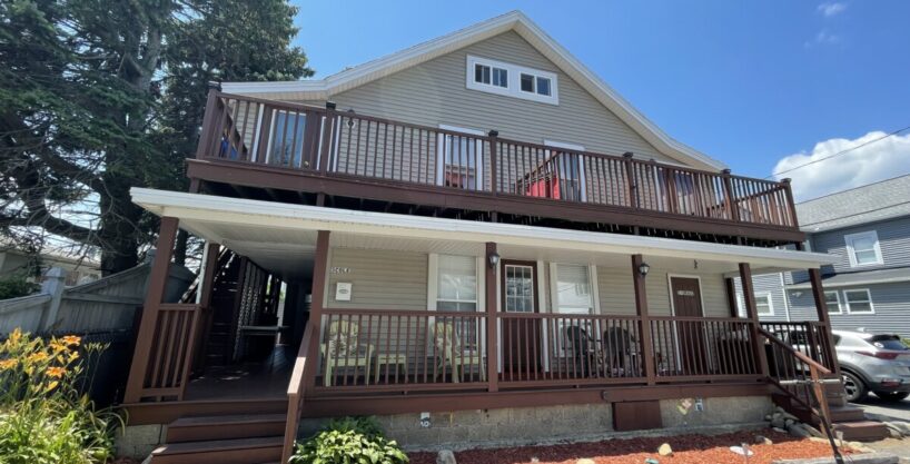 a two story house with a deck and a car parked in front of it.