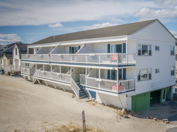 Beachfront multi-story residential building with balconies and ground-level parking.