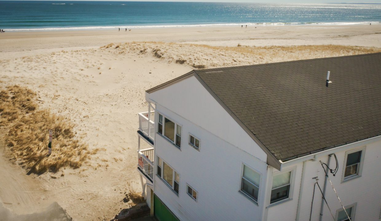 Aerial view of a coastal beach house with a vast sandy beach and ocean horizon in the background.
