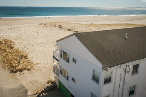 Aerial view of a coastal beach house with a vast sandy beach and ocean horizon in the background.