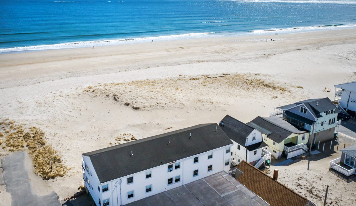 Aerial view of a coastal neighborhood with beachfront homes adjacent to a sandy beach overlooking the ocean.