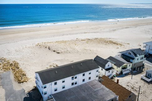 Aerial view of a coastal neighborhood with beachfront homes adjacent to a sandy beach overlooking the ocean.