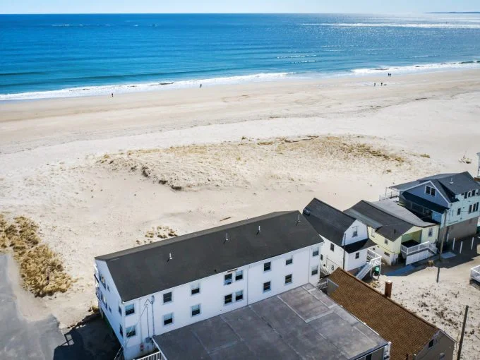 Aerial view of a coastal neighborhood with beachfront homes adjacent to a sandy beach overlooking the ocean.