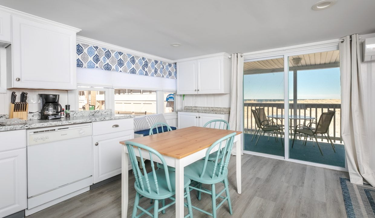 Bright, contemporary kitchen with white cabinets and blue backsplash, leading to a balcony with an ocean view.