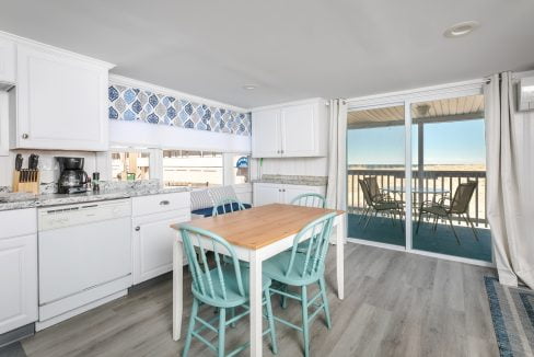 Bright, contemporary kitchen with white cabinets and blue backsplash, leading to a balcony with an ocean view.