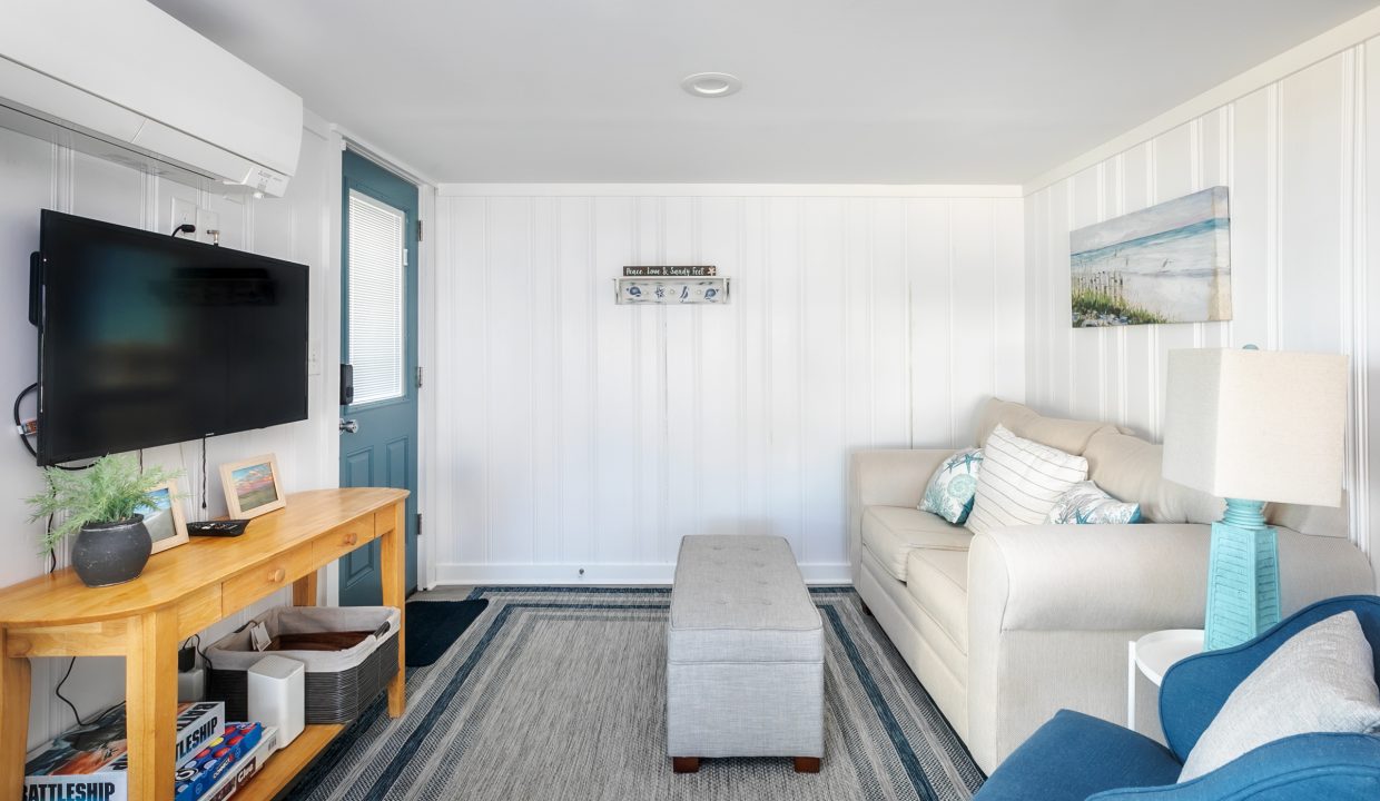 A bright, coastal-themed living room with a mounted tv, beige furniture, and nautical accents.